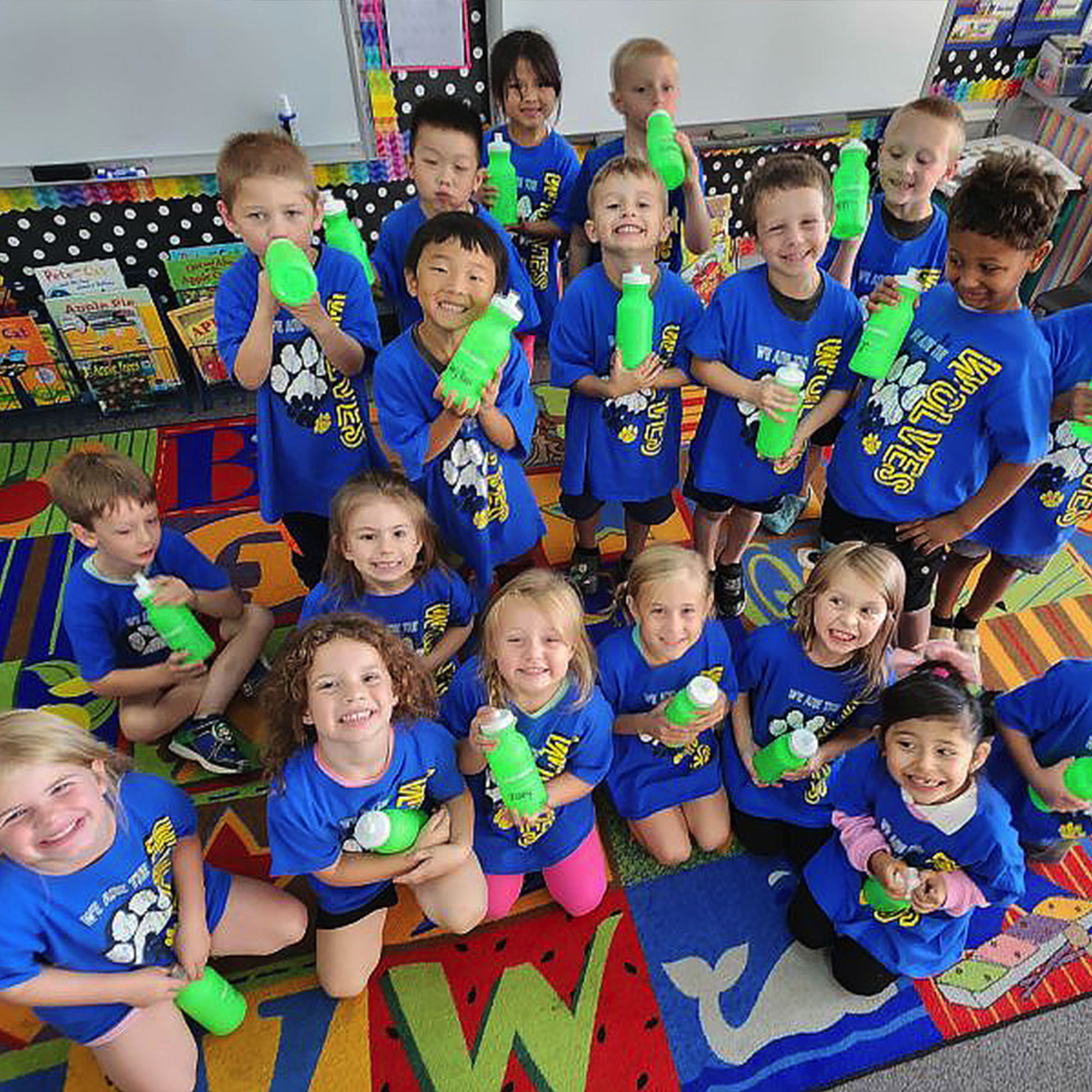 A cheerful group of children dressed in blue shirts, each with a green bottle, gathered in a playful setting.