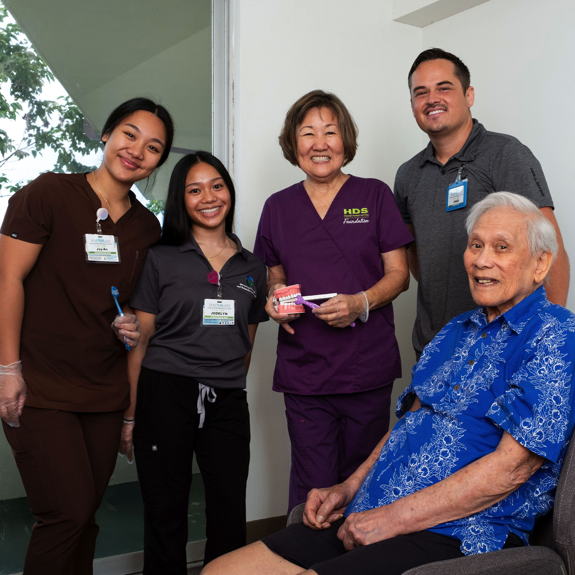 A older man on a chair in a dental office, accompanied by dentists.