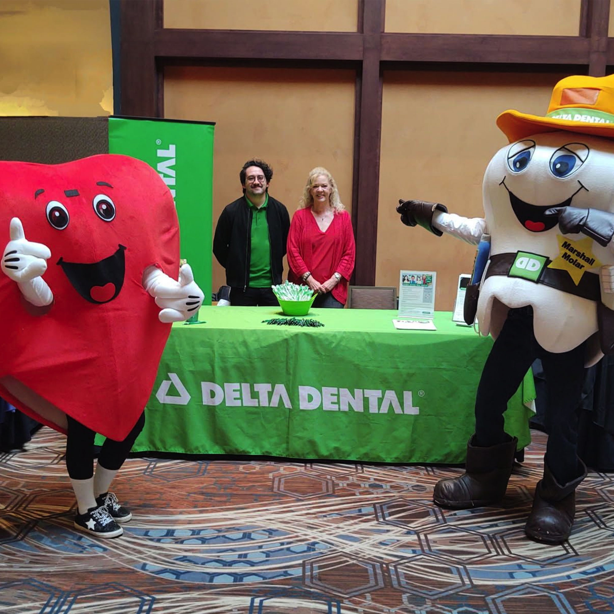 A tooth and heart mascot standing in front of a Delta Dental booth at a convention.