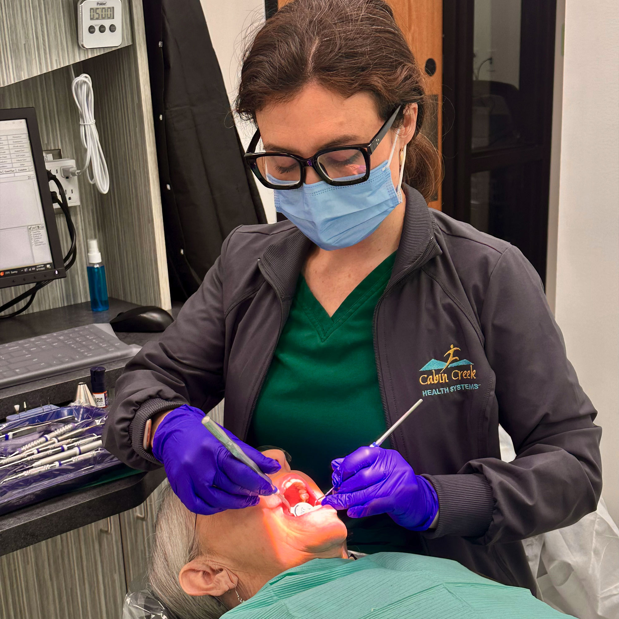 A woman wearing a blue mask and gloves is attending to a patient in a medical setting.