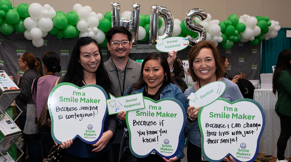 Three people hold signs that promote their role as smile makers in the oral health workforce.