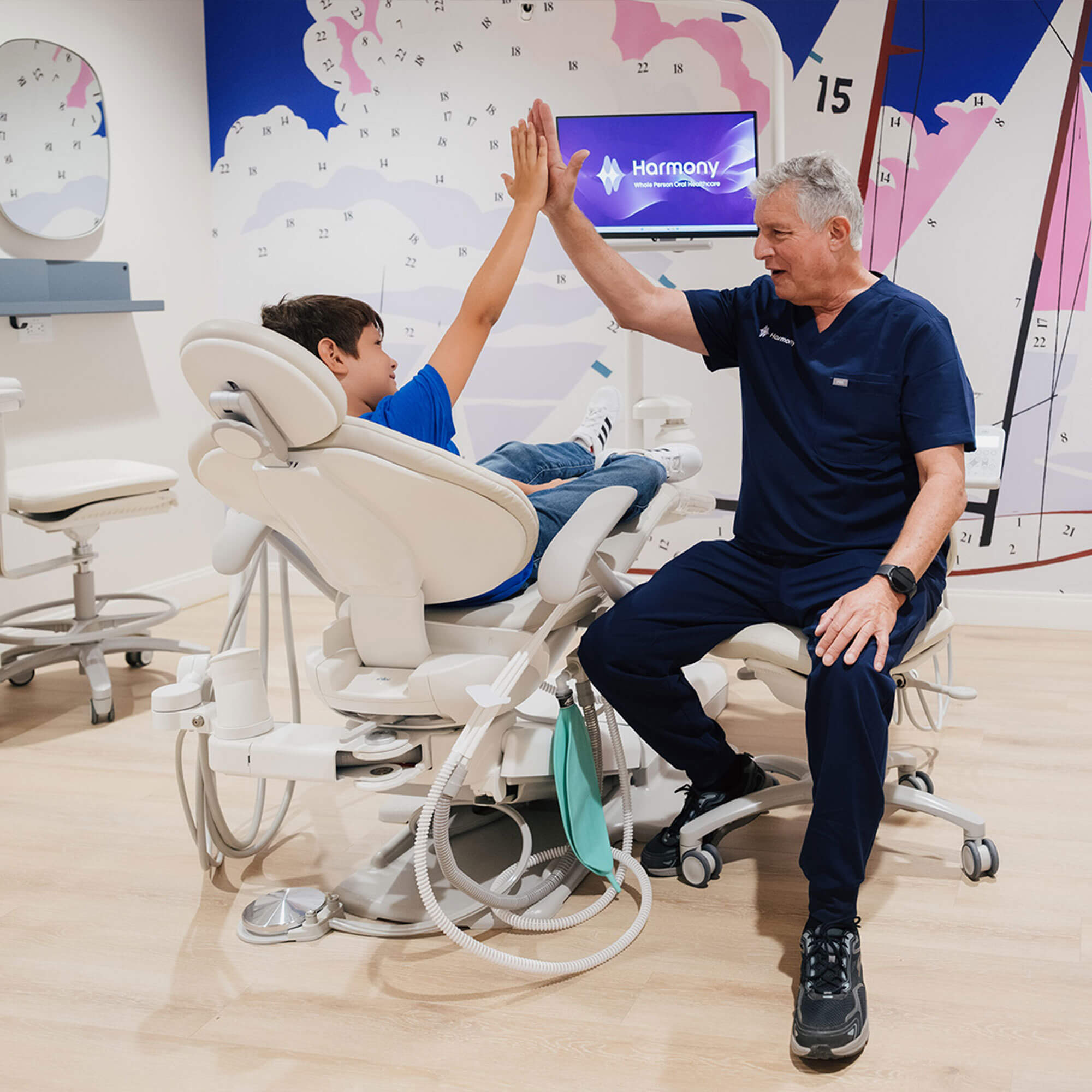 A boy sitting in a chair smiles as a dentist gives him a high-five.