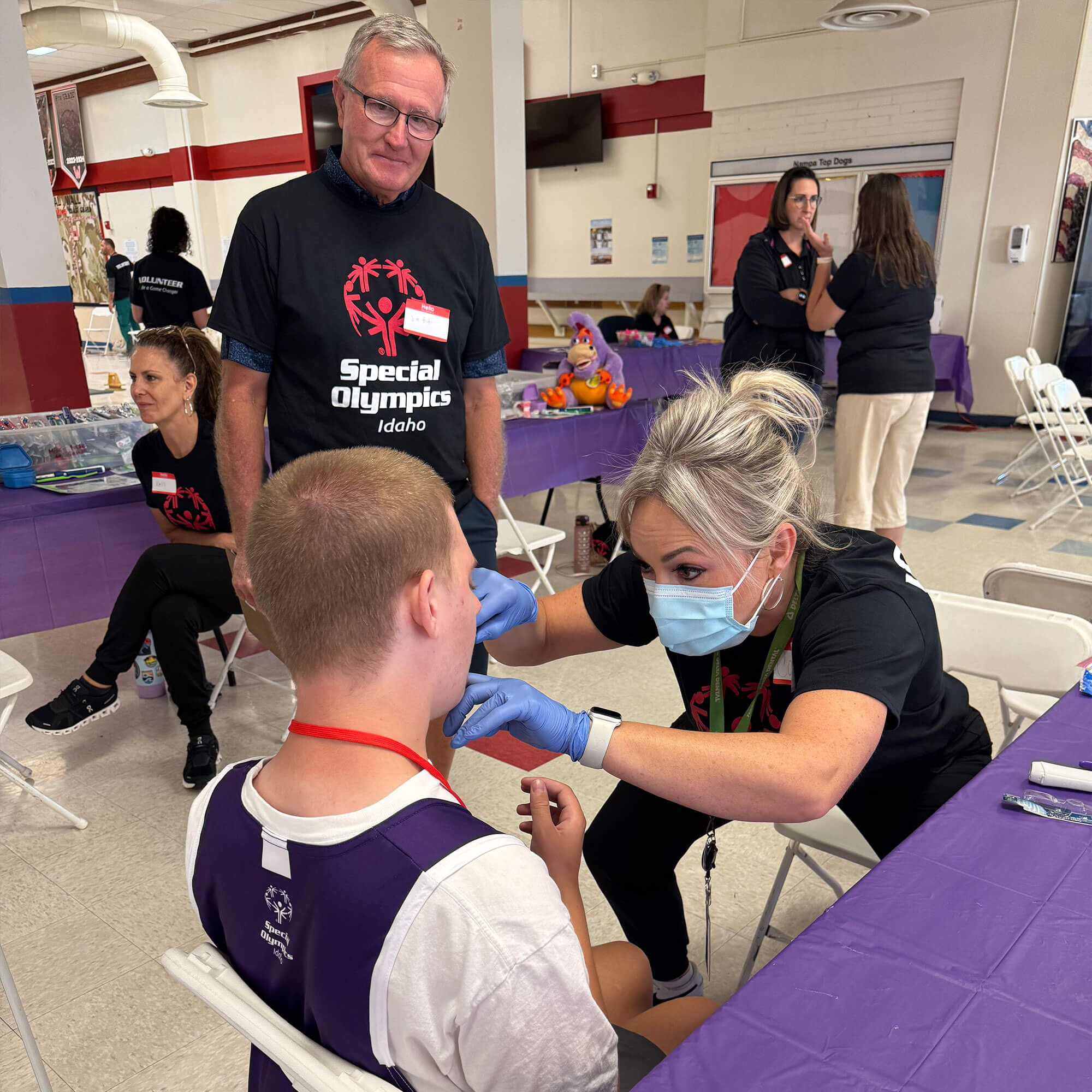 A woman wearing a blue mask and gloves is attending to a young patient in a school setting.
